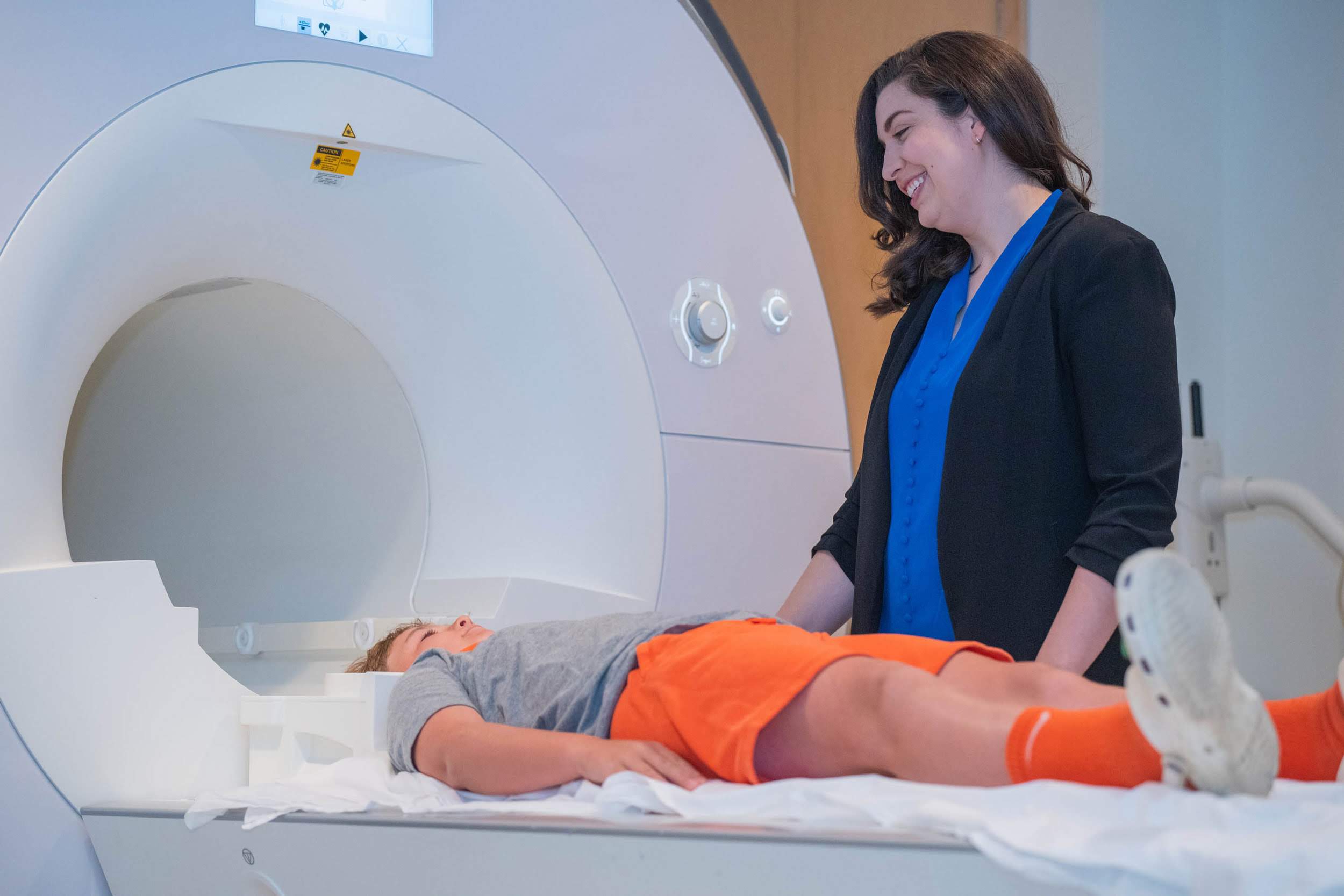 A researcher and child participant beside an MRI scanner
